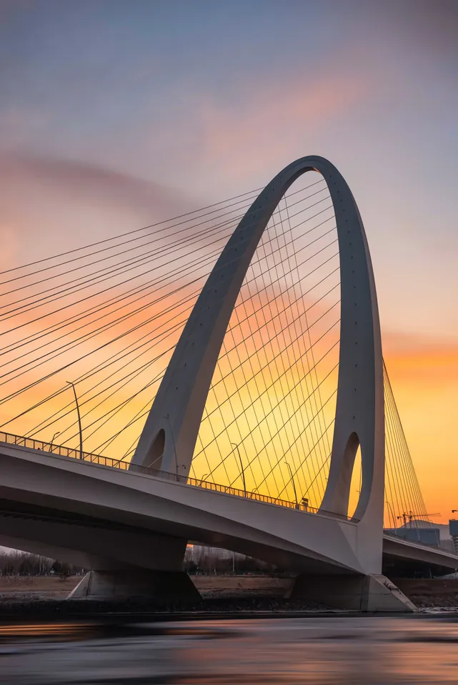 An illuminated arch bridge beneath a pink evening sky