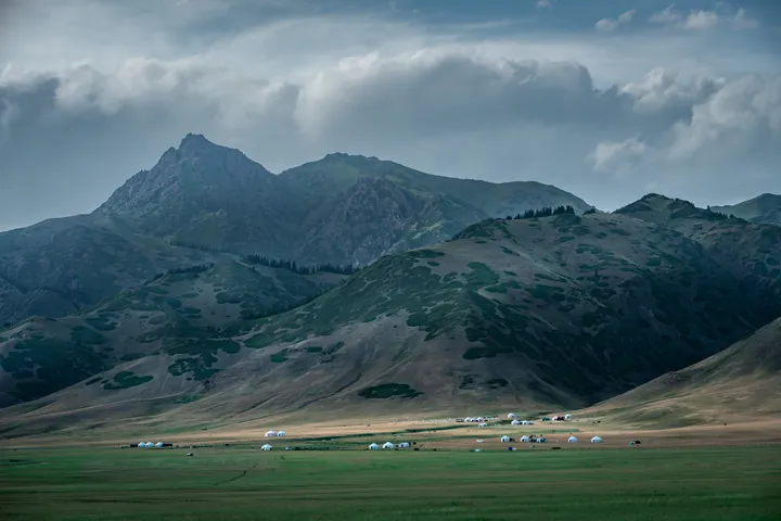 A mountain range above a green meadow under heavy clouds