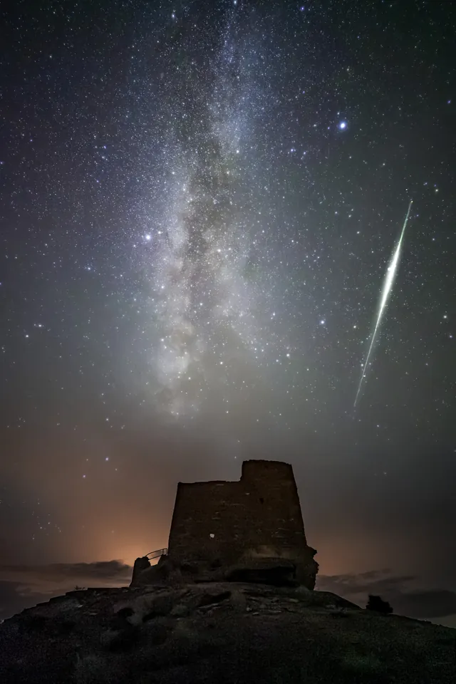 A bright streak beside the Milky Way above a stone tower