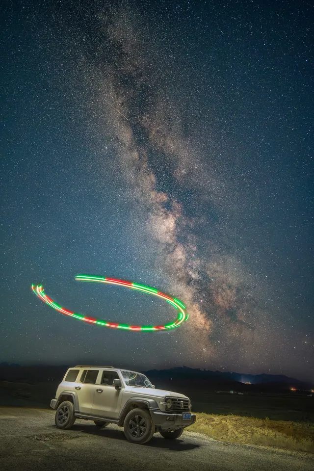 The Milky Way and a light trail above a parked vehicle